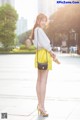 A woman in a white shirt and yellow skirt is standing on a sidewalk.