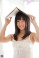 A woman in a white dress holding a book over her head.