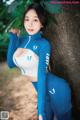 A woman in a blue and white outfit leaning against a tree.