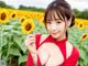 A woman in a red dress holding a sunflower in a field.