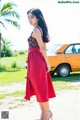 A woman in a red dress standing in front of a yellow car.