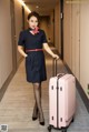 A woman in a blue dress holding a pink suitcase.