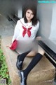 A woman in a school uniform sitting on a stone ledge.