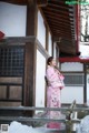 A woman in a pink kimono standing on a wooden bridge.