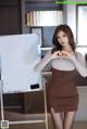 A woman in a brown dress standing next to a white board.