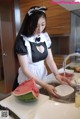 A woman in a maid outfit is washing a watermelon.