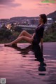 A woman sitting on the edge of a swimming pool at sunset.