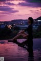 A woman sitting on the edge of a swimming pool at sunset.