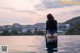 A woman sitting on the edge of a swimming pool looking out over the city.