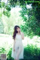 A woman in a white dress standing under a tree.