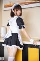 A woman in a maid outfit posing in a kitchen.