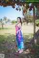 A woman in a colorful dress standing under a tree.