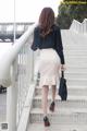 A woman in a black blouse and a white skirt is walking up some stairs.