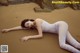 A woman laying on a sandy beach in a white bodysuit.