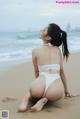 A woman in a white bikini sitting on the beach.