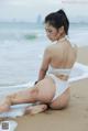 A woman in a white bikini sitting on the beach.