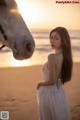 A woman in a white dress standing next to a white horse.