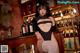 A woman in a black bodysuit and white stockings posing in front of a bar.