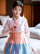 A woman in a pink and blue hanbok standing on a bed.