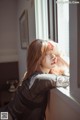 A woman leaning against a window with her hand on her head.