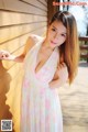 A woman in a pink dress leaning against a wooden wall.