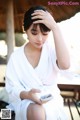 A woman in a white robe sitting on a bench looking at her cell phone.