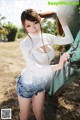 A woman in a white top and denim shorts posing in front of a tractor.