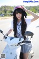 A woman in a school uniform is posing on a motor scooter.