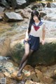 A woman in a sailor outfit sitting on a rock by a stream.