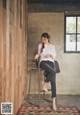 A woman sitting on a stool in front of a wooden wall.