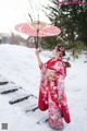 A woman in a red kimono holding an umbrella in the snow.