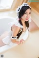 A woman in a maid outfit sitting in a bathtub.