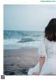 A woman in a white dress sitting on the beach.