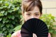 A woman holding a black fan in front of her face.